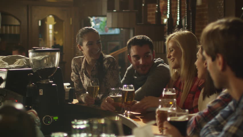 Friends do toasts, drink beer and cocktails while having a good time together at a bar. Shot on RED Cinema Camera in 4K (UHD).