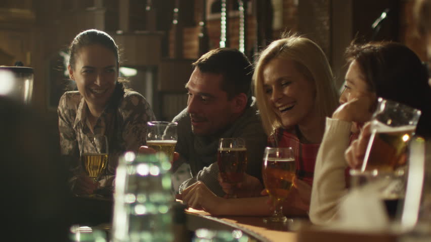 Friends do toasts, drink beer and cocktails while having a good time together at a bar. Shot on RED Cinema Camera in 4K (UHD).