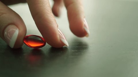 Woman hand with nail polish placing a red capsule on the table