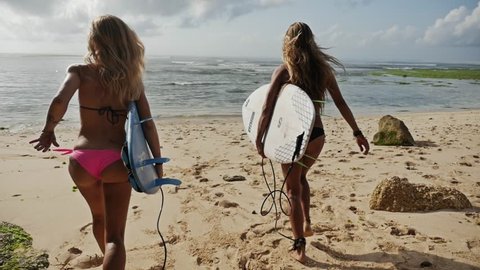 Two girls running into the ocean with their surfboards. Shot taken by a handheld gimbal in 50FPS.
