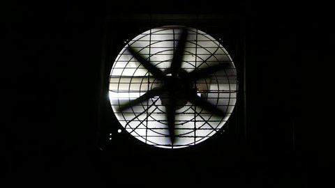 Exhaust fan on black wall, fan hole lit by the room lighting. Fan quickly rotates. pulling air from the room.