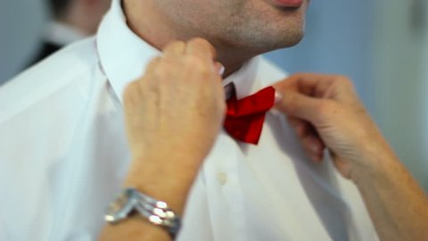 Mother helps adjust a red bow tie for a groom on his wedding day as cameras flash.