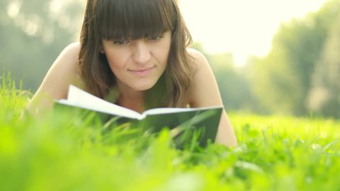Young attractive woman reading book on meadow, dolly shot