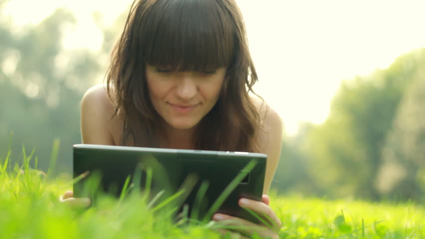 Young happy woman with tablet computer on meadow