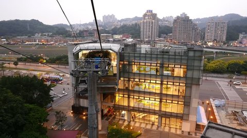 TAIPEI, TAIWAN - FEBRUARY 17, 2015: Warm window wall at lower terminal station, Maokong gondola lift. View from cabin move down, approach bright building, evening time, dusk aerial of Taipei suburb