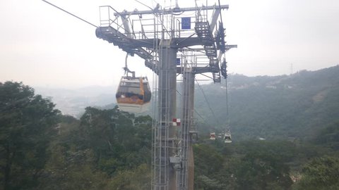 POV view Maokong gondola lift departs from station, dusk mountain landscape, evening twilight. Pass support pylon, steel cable driven carriage move forward, down hill slope.