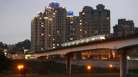 Night city, dusk view, metro train on bridge against urban landscape, Taipei Rapid Transit System (MTR) metro, elevated railroad part over canal, overground viaduct.