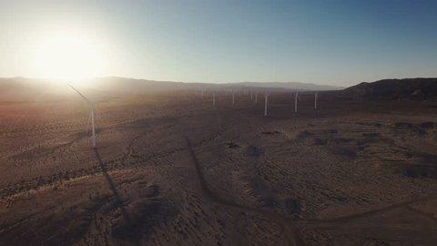 4K Aerial dramatic backward view through Wind Turbines in desert at sunset