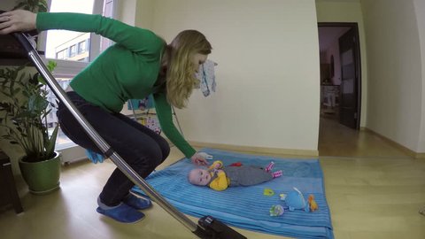 mother look after baby boy and clean home floor with vacuum cleaner. Wide angle shot. 4K UHD.