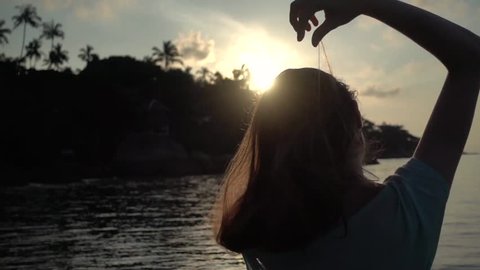 Girl smoothes her hair on a beach at sunrise