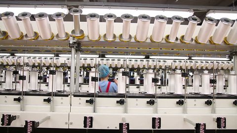 Textile fabric manufacturing machines in work. Woman working in factory. 
Cotton yarn production in a textile factory. Production of synthetic fibers in the textile industry. 