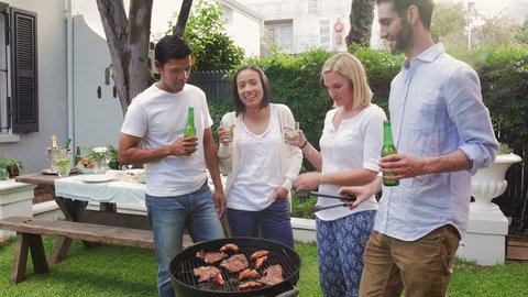 Diverse group of friends cooking meat on fire and drinking beers having fun together at garden party lifestyle weekend