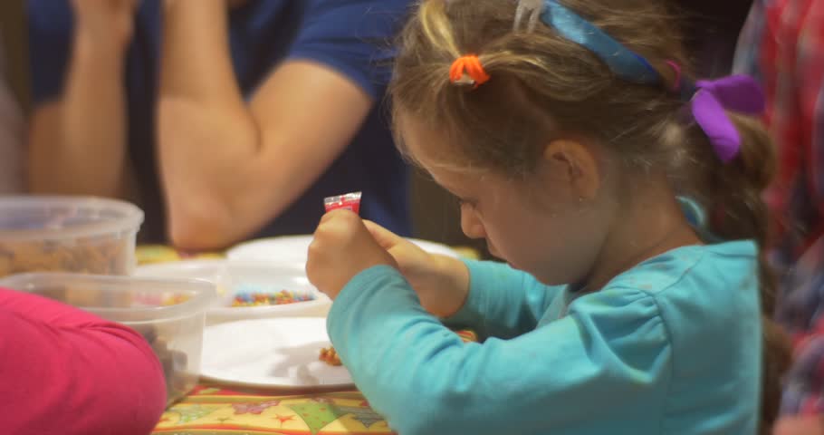Little Blonde Girl with Concentrated Face Puts a Pink Mastic From Tube to Cookie, Other Person Hands Put a Green Mastic to a Biscuit, Kids Children, family, People Are Standing at the Table, painting
