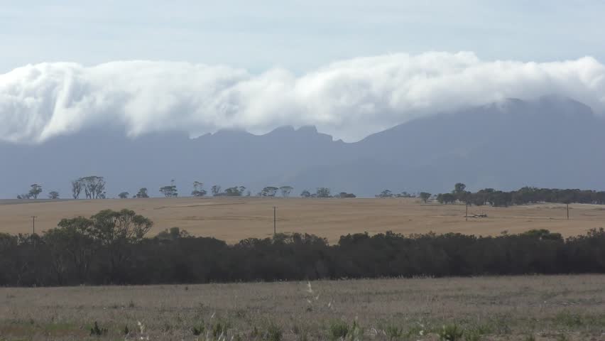 Scenic landscape with clouds covering Bluff Knoll mountain in Stirling Range National Park, Western Australia, wheat field in foreground, copy space.