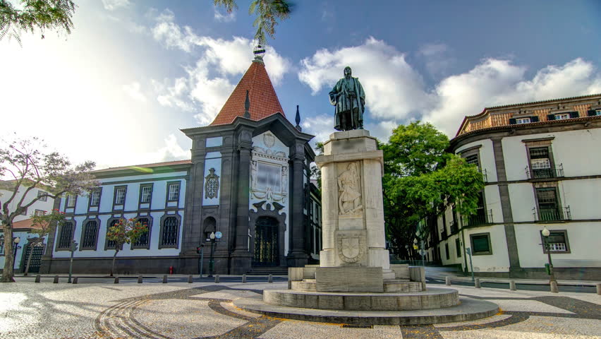 A statue of Zarco stands on the Avenida Arriaga timelapse hyperlapse and Banco de Portugal in the background in Funchal, Madeira, Portugal.