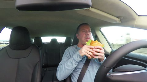 Careless man eating a sandwich while driving his car.  Safety note: this clip was carefully created in a controlled setting.