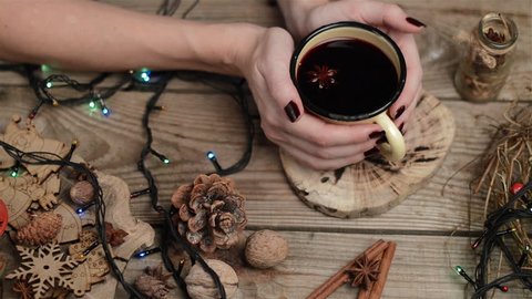 Woman hands holding holiday gluhwein in iron mug on wooden table with Christmas lights