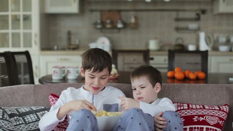 two boys eating popcorn on a sofa in the dining room