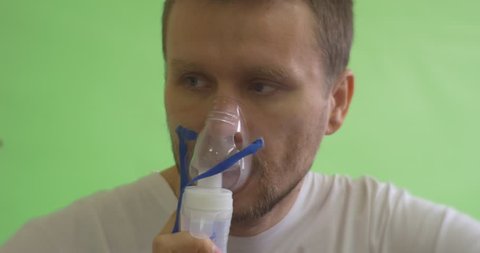 Man on Chroma Key, Green Screen, Patient in White T-Shirt is Keeping a Mask at His Face, takes away, tries to breath, put again, Breathing through Inhaler, Nebulizer, Steam from Nebulizer, breathing