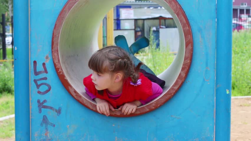 Little cute smiling girl play in tube on playground
