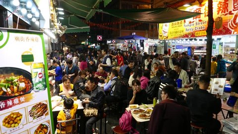 HONG KONG - FEBRUARY 21, 2015: Chinese open-air overcrowded restaurant on night street, Hong Kong city. Includes original sound. Noisy crowd of people eating, talking, resting.