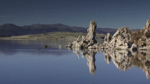 Two ducks boogie on a lake that mirrors a rock formation.