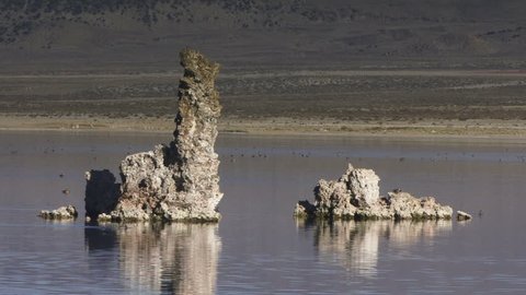 Ducks boogie along on a lake around two rock formations.