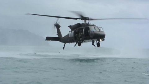 CIRCA 2010s - Paratroopers jump from a low flying helicopter into an ocean bay.