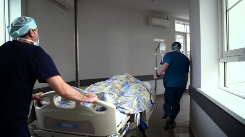 Patient on stretcher pushed at speed through a hospital corridor by doctors. In cart lies the educational dummy.