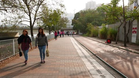 HONG KONG - FEBRUARY 21, 2015: Unidentified people walk along Tuen Mun river promenade, jogging, recreating, biking area. POV camera move forward, facing up different citizens on the way.