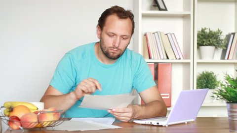 Worried man calculating bills by the table at home