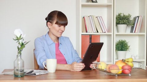 Young woman chatting on tablet computer by the table in home
