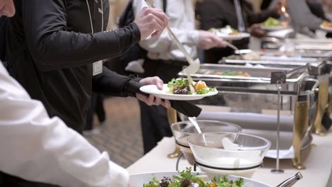 Guests attending a corporate business seminar in a hotel help themselves to the free lunch at the catered buffet table.