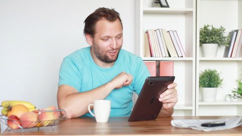 Young man chatting on tablet computer by the table in home