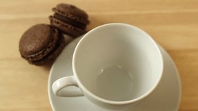 Coffee poured into a white cup on a wooden table with macaroons and cinnamon HD