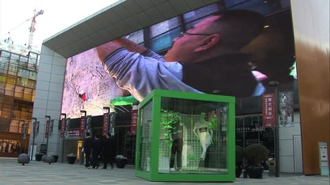 Beijing, China - March 2009: Large screen showing ads at the Taikoo Li shopping mall at Sanlitun, Beijing, China. Shoppers walking by.