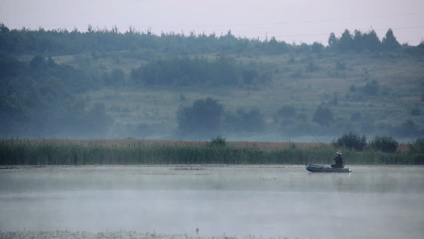 Fisherman on an inflatable boat in the early morning fishing on a lake. Mist rises over the water.