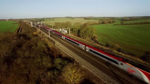Aerial shot of a fast Virgin passenger train in the UK countryside moving towards and then passing the camera, which is tracking backwards. Plenty of cutting room either side. 4K version ID 24513560