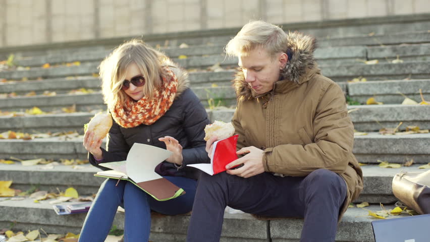 Students eating sandwiches and reading notes while sitting on the stairs
