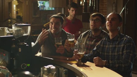 Friends are watching a sports game in a bar and cheering at a score. Shot in 4K (UHD).