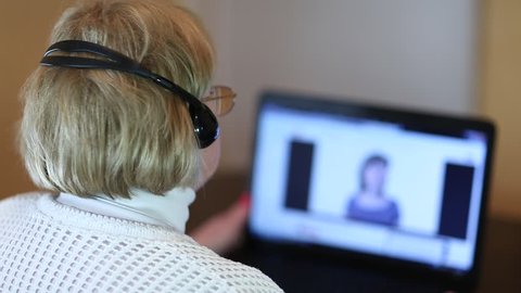 Woman with headphones with microphone talks to a customer via computer. Woman communicates via laptop. Senior woman with headphones and notebook speaks with customer