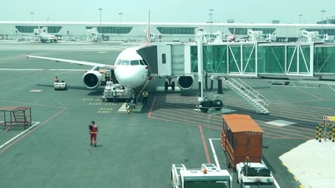 KUALA LUMPUR, MALAYSIA - MARCH 07, 2015: Aircraft approach and stop at apron, jet bridge attached, passengers go out by aerobridge, front view time lapse shot. Airliner surround by ground personnel