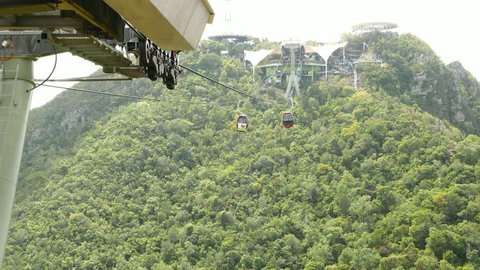 Langkawi gondola lift move away against woody slope, time lapse shot. Small cabin suspended on steel cable, quickly slide away from middle station. Mountain landscape green slope.