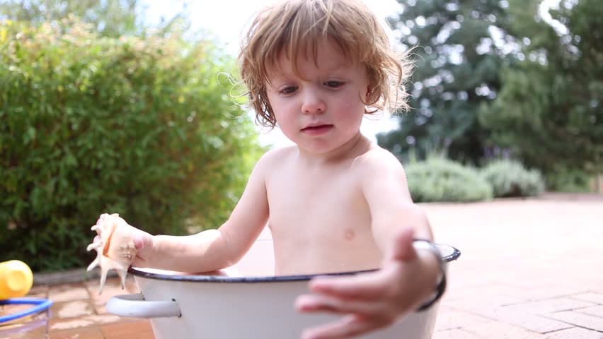Toddler boy bathing outside in bucket