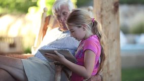 Pre-teen girl showing her grandfather a video on a tablet