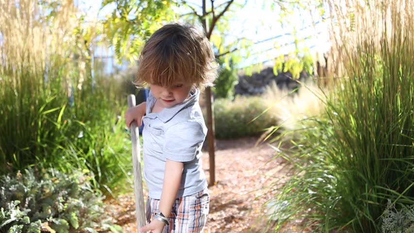 Toddler boy playing with a rake outside