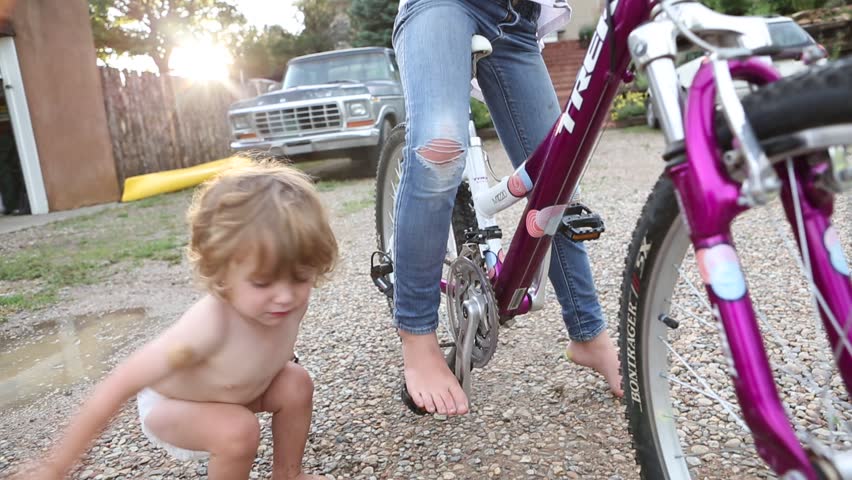 9 year old girl biking and 2 year old toddler boy playing in parking lot