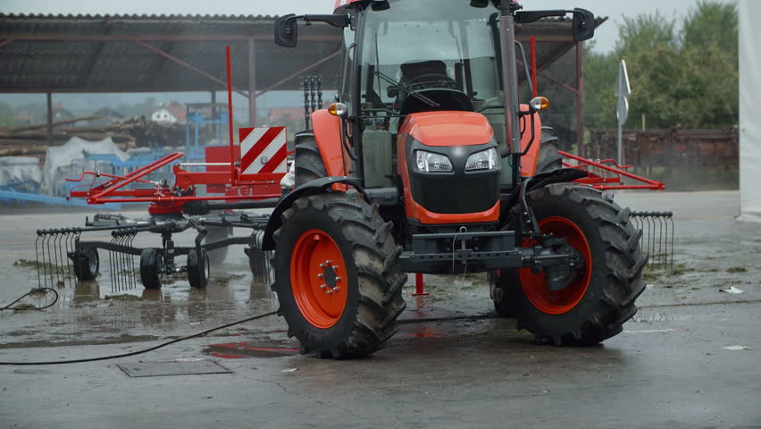 In this video, we can see that a tractor is parked outside in the parking lot in front of the factory where it was produced. Close-up shot.