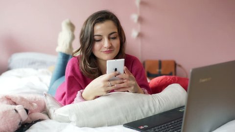 Teenage girl texting on smartphone and checking something on laptop
