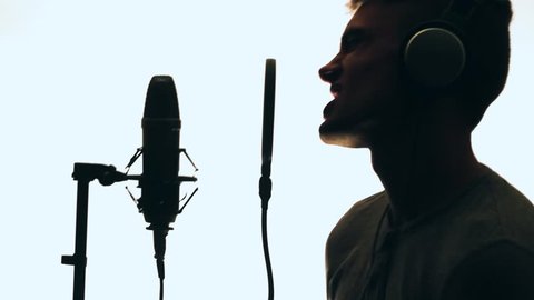 Handsome Guy Singing Into a Microphone Standing backlit. Recording studio. Man silhouette.